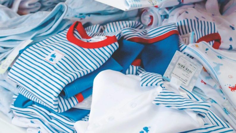 A variety of cute, colorful baby clothes neatly arranged on a store shelf.